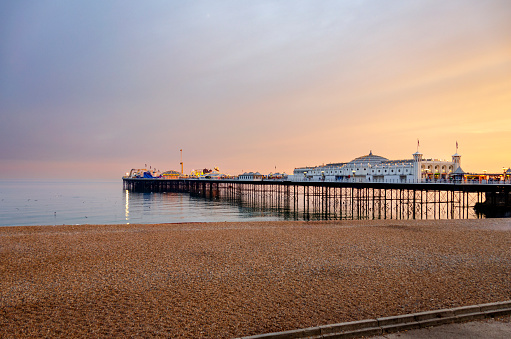 The picturesque Brighton beach at sunset, where the fading light casts a warm glow over the pebbled shore. Brighton is famous for the Brighton Pier which extends into the sea, creating a classic and beloved scene along the English coast.