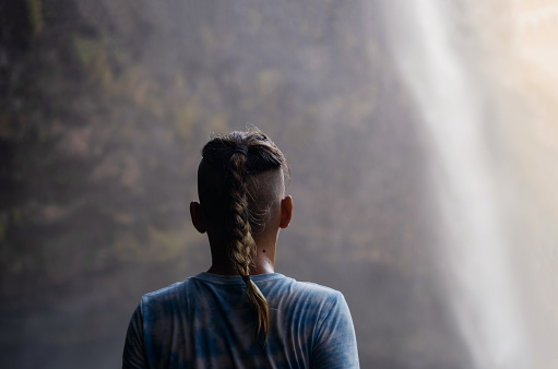 Teenager looking as waterfall cascades in front of him.