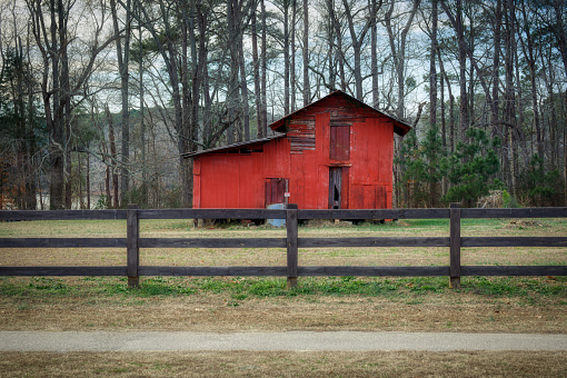 A little red barn landscape centered behind a wooden fence in Winter in North Carolina, USA.