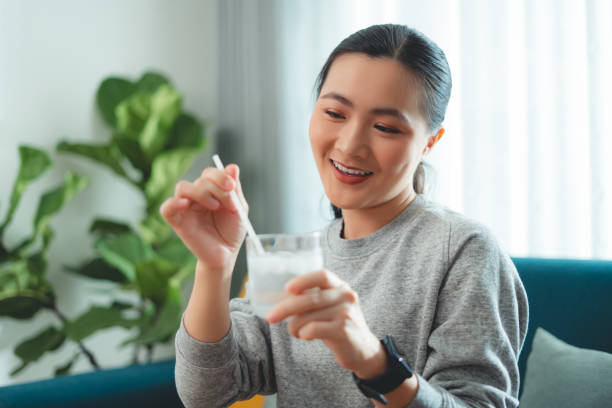 istock Asian woman relaxing taking a break using straw stirring water with ice, sitting on sofa in living room. 1903727436