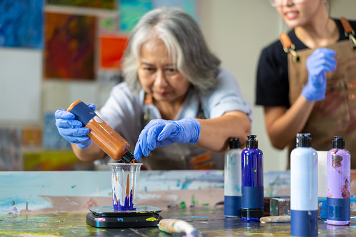 4K Group of Happy Asian senior people learning acrylic pouring art workshop at art studio. Elderly retired man and woman enjoy and fun with colorful abstract modern art painting in classroom.