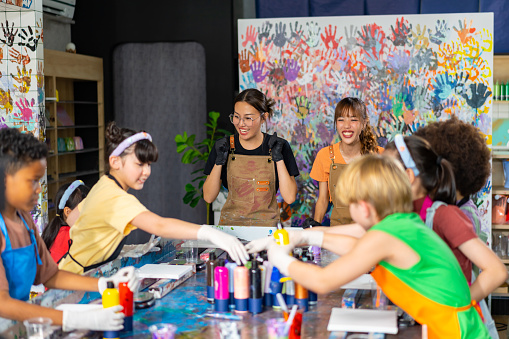 Group of Diversity school children learning acrylic pouring art on canvas workshop with teacher at art studio. Happy boys and girls enjoy and fun with colorful abstract modern art painting in classroom.