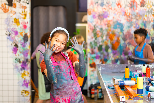 Portrait of young Asian girl learning acrylic art workshop with friends at art studio. Happy boys and girls enjoy and fun with colorful abstract modern art painting in classroom.