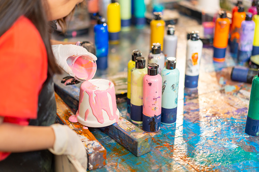 Group of Diversity school children learning acrylic pouring art on pottery workshop with teacher at art studio. Happy boys and girls enjoy and fun with colorful abstract modern art painting in classroom.