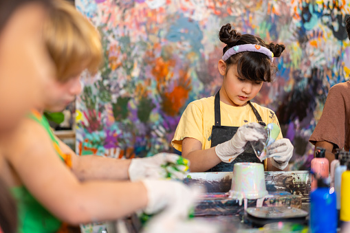 Group of Diversity school children learning acrylic pouring art on pottery workshop with teacher at art studio. Happy boys and girls enjoy and fun with colorful abstract modern art painting in classroom.