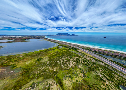 High view of Cape Town’s West Coast wetlands, Rietvlei and Sunset Beach coastline, with Table Mountain in backdrop. Wetlands nature reserve in foreground.