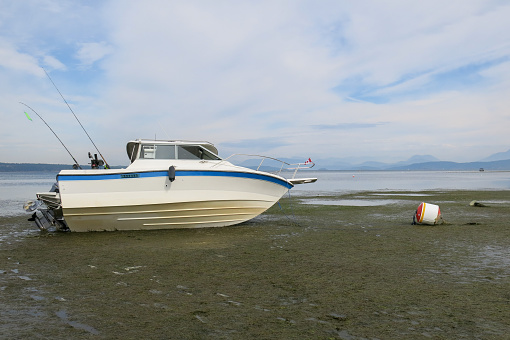 A small fishing boat is beached on a mooring ball at low tide.
