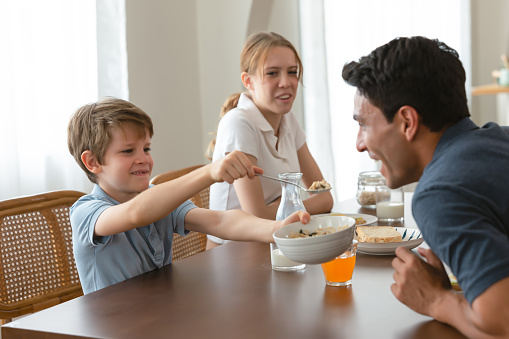 Funny family Caucasian morning. Happy little boy with family have fun breakfast. Little son feeding his father with spoon in kitchen. Trusting relationship between child and parent. Focus Child