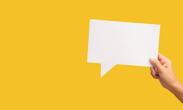 Hand holding a blank white speech bubble against a yellow background. Space for text