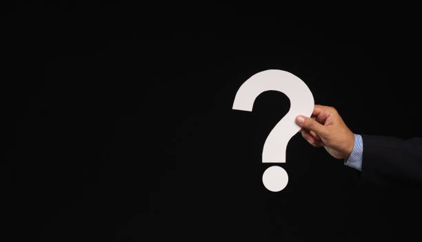 istock Hand holding a white question mark symbol against a black background. 1903870394