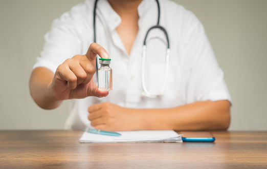 A Physician holds a vaccine bottle while sitting at the table in the hospital. Concept of medical and healthcare