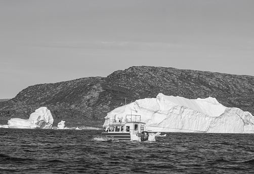 A pleasure boat powers among floating icebergs in Disko Bay, Western Greenland.