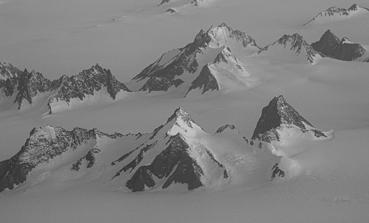 A black and white aerial study of newborn mountains (nunataks) emerging from the ice sheet in Eastern Greenland.