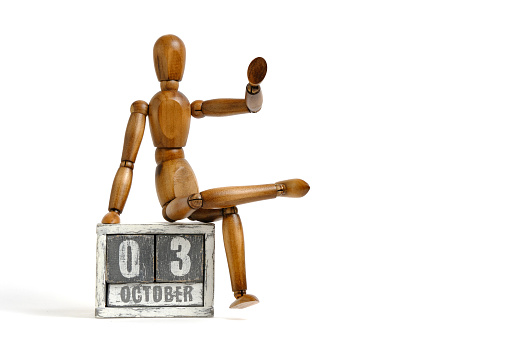 October 03, wooden calendar with mannequin sitting on it on white background. Calendar date