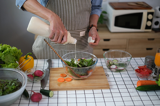 Cropped shot senior man pouring sauce into bowl with fresh salad. Healthy eating and culinary concept