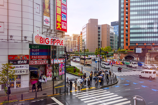 AKIHABARA, TOKYO, JAPAN - NOVEMBER 12, 2023: The lively view of the colorful billboards on the buildings in the Akihabara Electric Town in Tokyo. People waiting to cross the street on a rainy day.