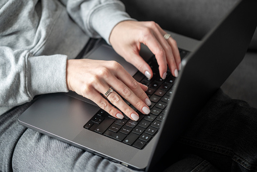 Working at home. Close-up of a young woman sits on a sofa and surfing the web with a laptop.