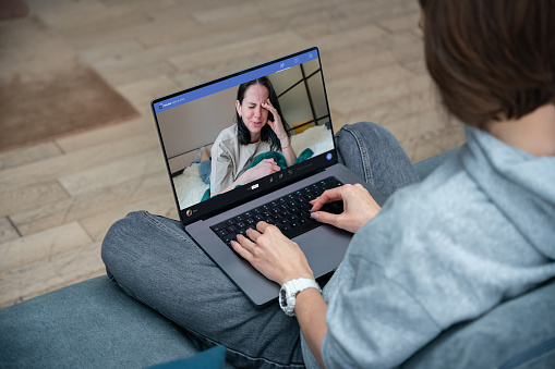 Young woman using laptop for video call with girlfriend. Depressed crying woman on the laptop screen, psychotherapy video call