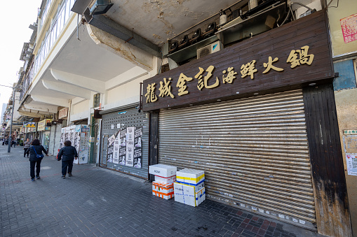 Hong Kong - December 31, 2023 : Pedestrians walk past closed stores in Kowloon City, Hong Kong.