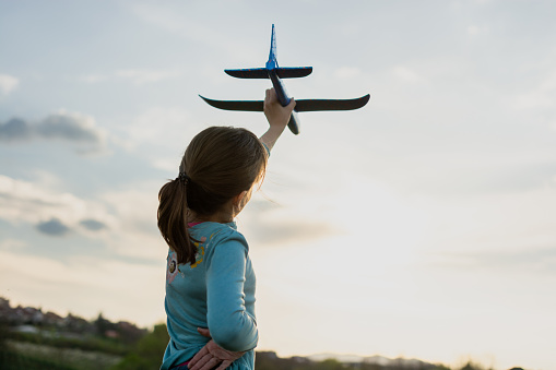 Rear view of a girl playing whit toy plane outdoors. She is holding a plane against a sky.