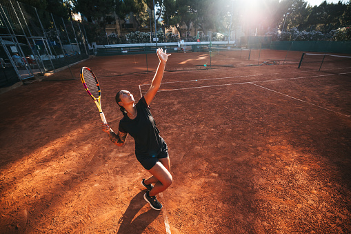 Woman tennis player on service on a outdoor clay court.