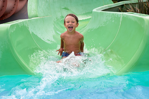 Kid descends from the water slide in the summer in the water park, happy child in the amusement park, summer family vacation