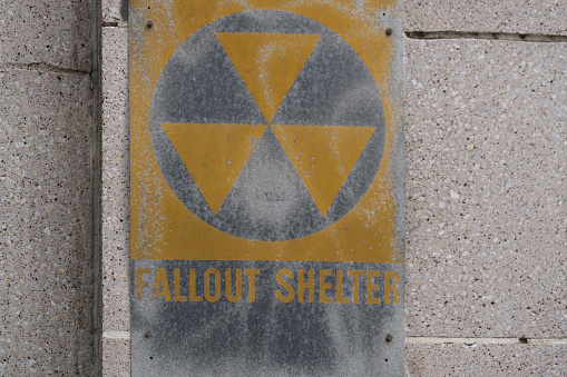 This stark yellow fallout shelter sign serves as a reminder of past anxieties, etched on a weathered concrete wall, evoking historical contemplation.