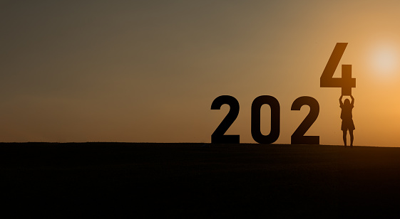 Woman holding standing happy new year 2024 concept, silhouette of woman stand lawn and success with beautiful sunset background. Happy New Year 2023 use for web banner and advertisement.