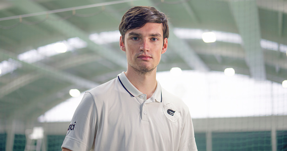Portrait of young male tennis player standing in tennis court.