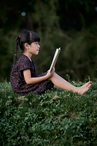 Little girl sits and reading a book in the green rainforest