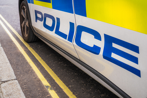 Close-up on the word 'Police' on the lower section of the side of a police car stopped on the street.