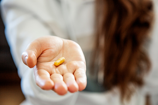 Close-up of a young woman holding a pill capsule in her hand.