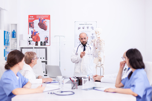 Expert radiologist demonstrating on skeleton during briefing with medical staff in hospital meeting room. Clinic therapist talking with colleagues about disease, medicine professional