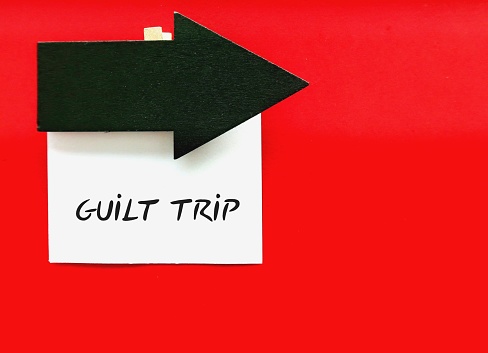On copy space red background, direction arrow with handwrtten note GUILT TRIP, to manipulate or cause another person to feel guilt sense of responsibility and change behavior