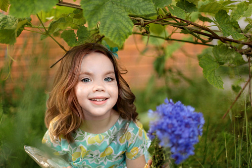 Little happy girl holding a lilac branch, purple flowers on the bush, spring mood, child in the park. High quality photo
