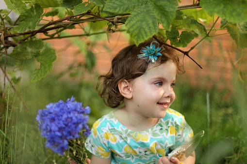 Little happy girl holding a lilac branch, purple flowers on the bush, spring mood, child in the park. High quality photo