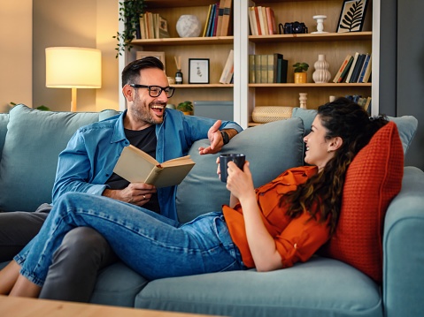 Man reading book, woman listens and enjoys in the living room together at home