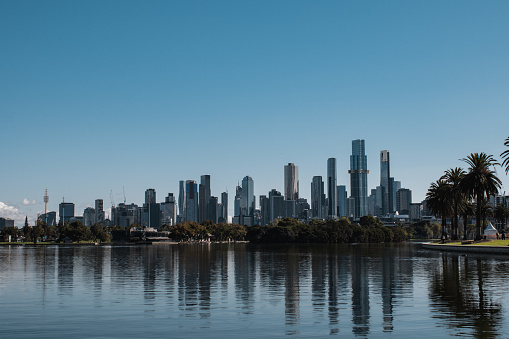 Melbourne City skyline from Albert Park on an autumn morning. The skyline reflects clearly onto the lake with the Australian Grand Prix circuit to the right.