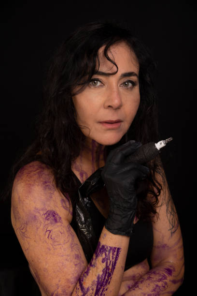Beautiful artist holding tattoo machine looking at camera against black background