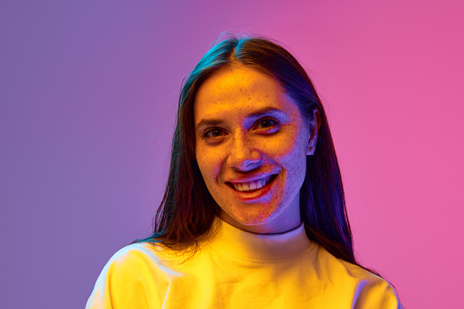 Close up portrait of positive, smiling beautiful woman with freckles against gradient purple pink background. Concept of beauty, youth, human emotions, self-expression fashion, fun and joy.