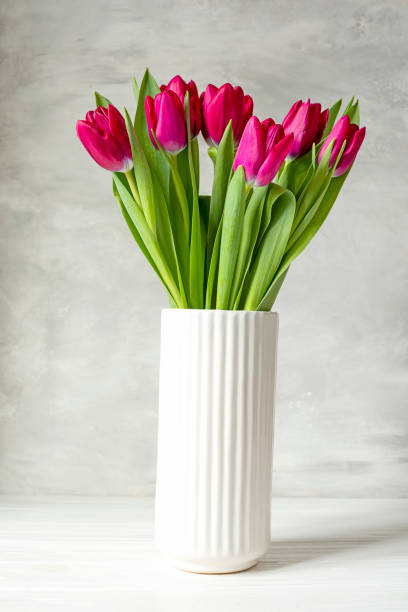 istock Ceramic white vase with burgundy tulips on a light wall background 1904390059