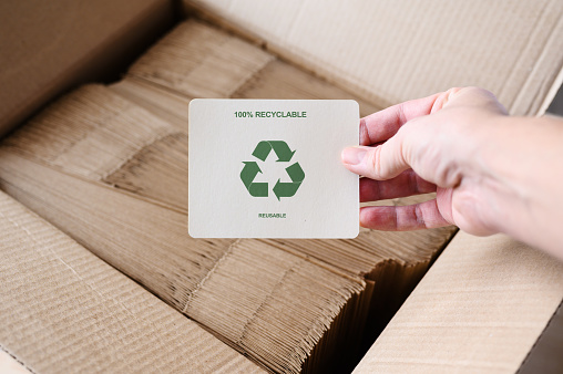 A sign with a recycling sign in a hand against the background of a box with paper bags. Production and sale of environmentally friendly packaging. Environmental protection concept