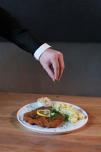 Schnitzel menu in stylish restaurant.  Man pours spices on food.