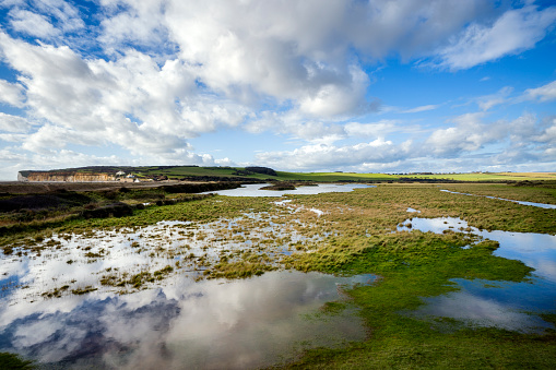 Evidence of flooding at Cuckmere Haven showing a large body of water in the foreground, with a big sky and cliffs in the distance.