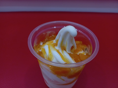 Simple ice cream sundae with mango topping and red background.
