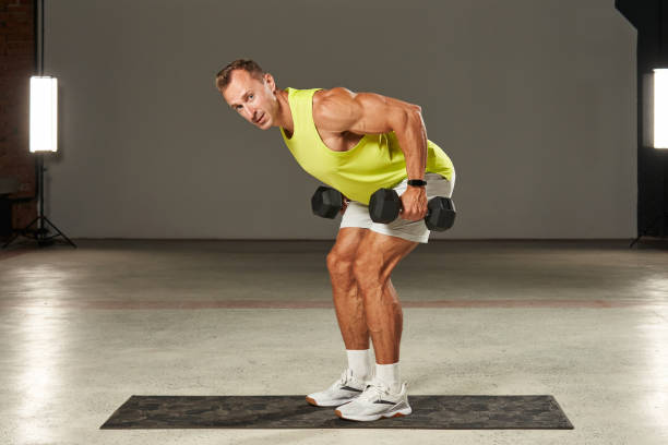 istock young Caucasian athlete doing dumbbell rows to the chest while standing on the floor. beautiful muscles of the arms and legs are tense 1904452027