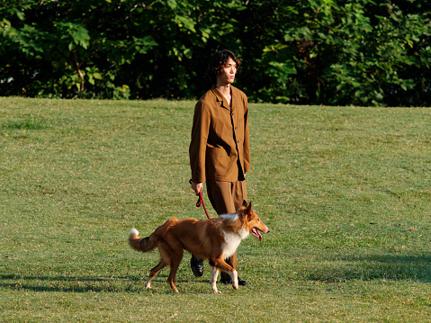 Portrait of a handsome Chinese young man walking with his rough collie dog on green grass field in sunny day, male fashion, cool Asian young man lifestyle, harmony man and pet.