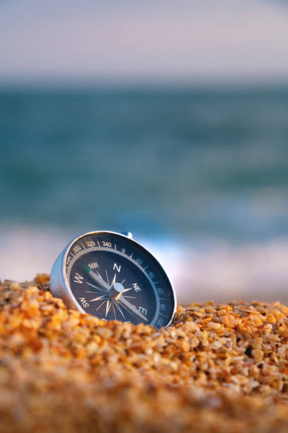 zdjęcie koncepcyjne, zbliżenie kompasu leżącego w mokrym piasku składającym się z małych okruchów muszli, na tle błękitnego, spokojnego morza - compass exploration the way forward beach zdjęcia i obrazy z banku zdjęć