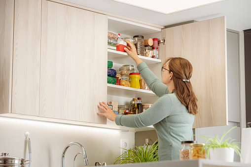 Woman arranging groceries in upper kitchen cabinet