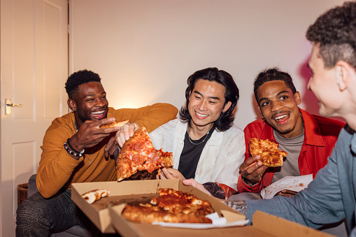 A group of young men enjoying a party at a house in North Shields, North East England. They are all socialising together, eating pizza.